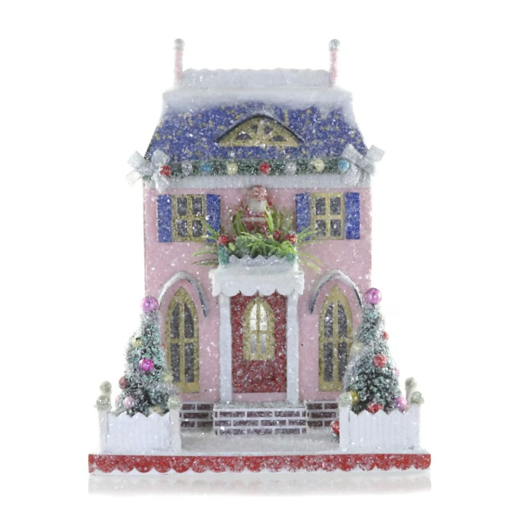 Pink glittered cardboard Santa cottage with blue snowy roof, shutters, and white fence.
Christmas village cottage with Santa above the doorway, decorated trees, and frosted sparkle.
Pastel holiday cottage decoration measuring 8.5 x 6.5 x 11 inches.