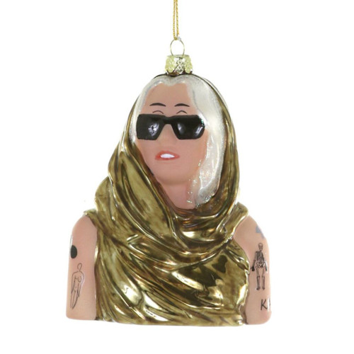 Glass pop-star bust ornament with black sunglasses and blonde hair.
Music-themed hanging ornament with gold draped outfit and tattoo-style arm details.
4.25 inch Miley Cyrus glass ornament on a white background.