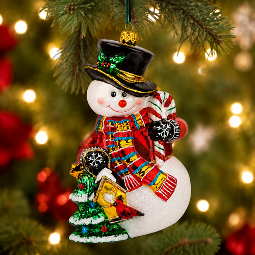 Huras Family 6-inch handblown glass Snowman with Christmas Tree ornament.

Polish glass snowman ornament with black top hat, red sweater, colorful scarf, glittered candy cane, and Christmas tree.

Glittered snowman Christmas ornament beside a green tree and snow-covered birdhouse with a red cardinal.