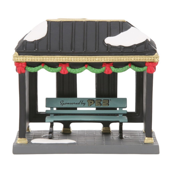 Department 56 Christmas In The City A Tasty Sponsor bus stop accessory with PEZ bench, black shelter, garland, and snow.
Vintage PEZ-sponsored bus stop with teal bench, gold trim, red-and-green holiday garland, and advertising panel.
Rear view of Department 56 bus stop accessory showing open shelter windows, snow patches, black roof, and festive trim.