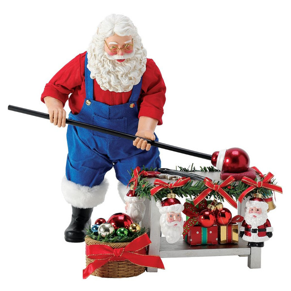 Possible Dreams Hand Blown Keepsakes Santa figurine creating Christmas ornaments at a festive workshop bench.
Santa in blue workshop overalls with Clothtique fabric, surrounded by ornaments, garland, and wrapped gifts.
10-inch hand-painted Department 56 collectible featuring handcrafted holiday keepsakes.