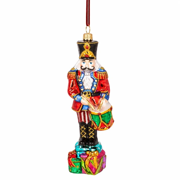 Huras Family Viennese Nutcracker 6.5-inch handblown glass Christmas ornament.

Polish glass nutcracker ornament in a red and blue uniform with gold details, black hat, boots, and colorful drum.

Hand-painted nutcracker Christmas ornament standing on colorful wrapped gifts and holding a red and green drum.