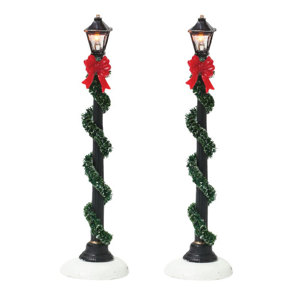 Set of two Department 56 Small Town Street Lamps with illuminated lanterns.
Battery-operated village lamps wrapped in green garland with festive red bows.
Department 56 village lighting accessories measuring 4.5 inches tall.