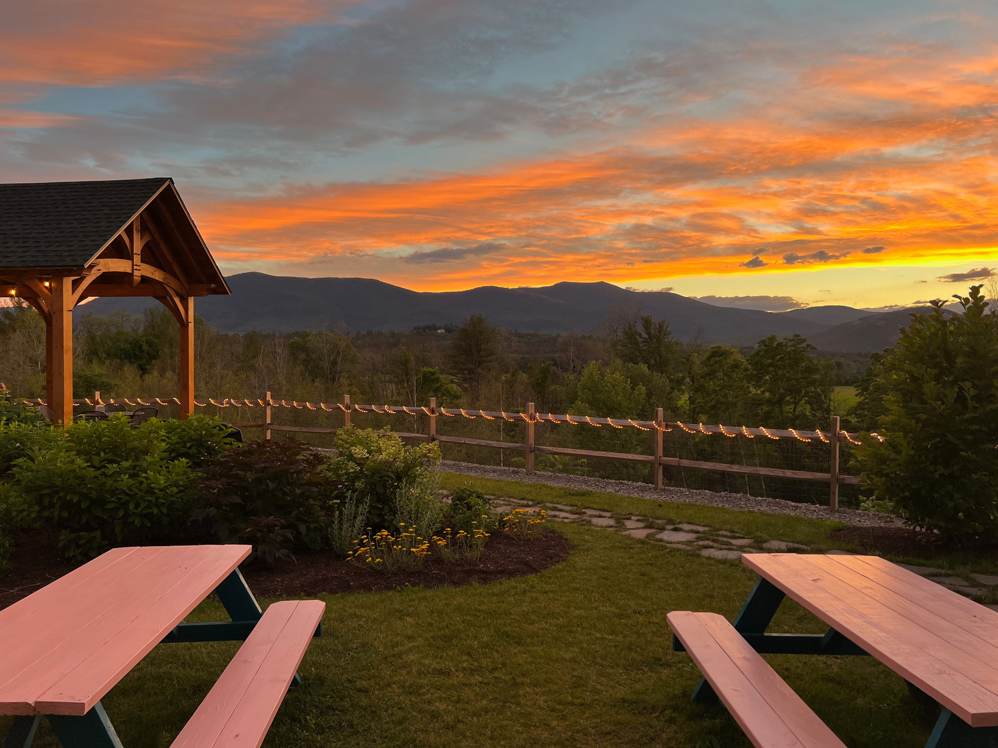 Scenic sunset view of the White Mountains from the patio at The Christmas Loft and Tricks And Treats located at 2028 White Mountain Highway North Conway NH. Featuring picnic tables, gardens, and coverage.