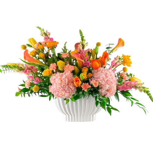 A vibrant blend of tangerine, golden-orange, and soft blush-pink blooms, complemented by lush greenery. This elegant arrangement brings warmth, colour, and seasonal charm to any occasion.