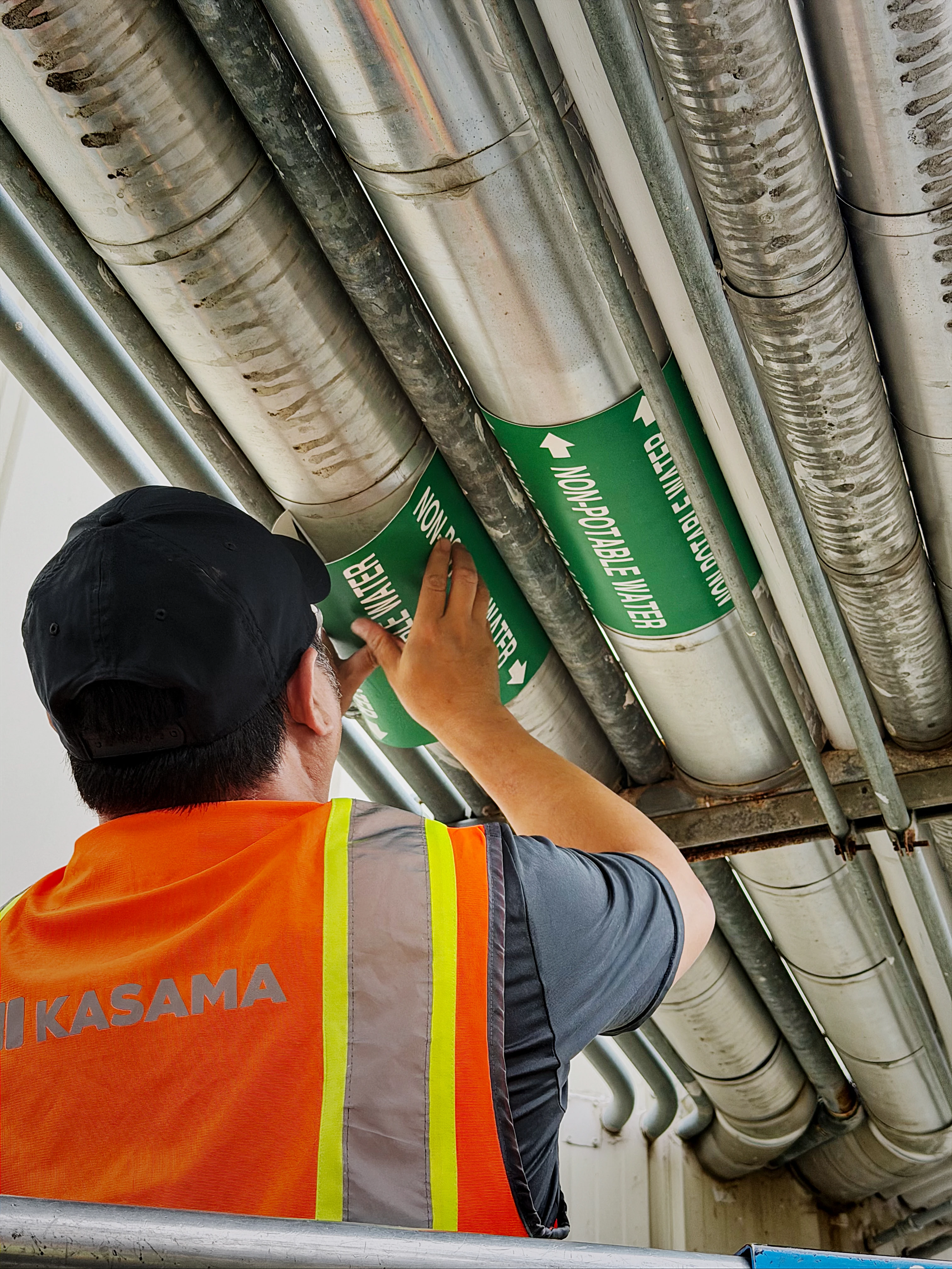 Color-coded ANSI/ASME A13.1 pipe markers with legends and flow arrows on facility piping