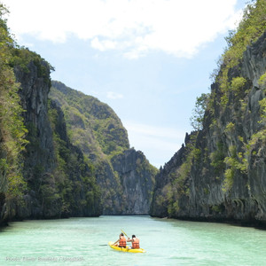 Two kayakers paddling into the Big Lagoon between steep limestone walls at El Nido, Palawan