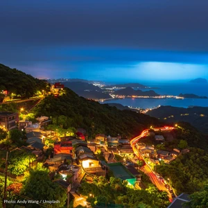 Jiufen's hillside lanes lit up at dusk above the north coast of Taiwan, with the sea and coastal lights beyond.
