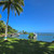 A palm-fringed Fijian lagoon on a clear blue-sky day, with two small day-tour boats moored in calm shallow water and an offshore island in the distance — illustrating Fiji's easy, family-ready Pacific holiday character.