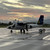A Solomon Airlines Twin Otter light aircraft on a wet runway tarmac at sunset, mountains in the distance — illustrating the internal light-aircraft legs that connect Honiara to the dive lodges of the Solomons.