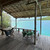 A timber-deck lodge platform in the Solomon Islands with a hammock chair and a small table set above a turquoise lagoon, looking out to mangrove-fringed islets — illustrating the off-grid, low-key Solomons lodge experience.