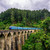 Sri Lanka's blue train crossing the stone arches of the Nine Arch Bridge near Ella, surrounded by green hill-country forest.
