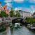 The white stone Triple Bridge arching over the Ljubljanica River in Ljubljana, Slovenia, with the pink Franciscan Church and pastel old-town facades behind.