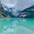 Canoeists paddling red canoes across the still turquoise water of Lake Louise on a misty morning