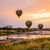 Three hot air balloons drifting at dawn over a rocky river winding through the savanna