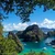 Outrigger boats moored below a limestone peak, seen through trees from a viewpoint above Coron, Palawan