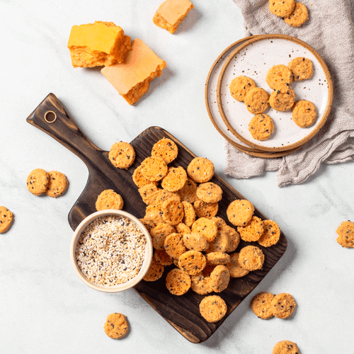 Everything cheddar biscuits on wooden board with bowl of everything bagel seasoning and three blocks of cheddar cheese and plates with scattered biscuits and napkin overhead Everything cheddar biscuits on wooden board with bowl of everything bagel seasoning and three blocks of cheddar cheese and plates with scattered biscuits and napkin overhead