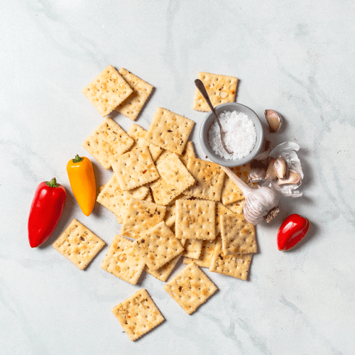 Large cocktail crackers scattered with red and orange pepper and salt in bowl with spoon and garlic overhead Large cocktail crackers scattered with red and orange pepper and salt in bowl with spoon and garlic overhead