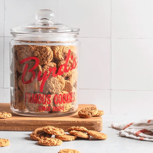 Filled glass Byrd's famous cookies cookie jar with cookies on wooden board with dish towel Filled glass Byrd's famous cookies cookie jar with cookies on wooden board with dish towel