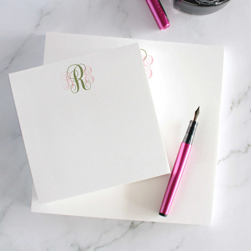 Traditional Script square notepads with a small green script monogram, beside a pink pen.