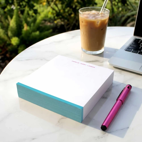 Modern Border square notepad with turquoise edges, on an outdoor table beside iced coffee.