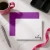 Holla Swash flat notecard with rounded corners and black Riley script, violet envelope, pink coffee mug, silver pen, ribbon and black desk tray.