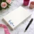 Holla Swash rectangular desk notepad with a royal-blue script name in the lower-left corner, beside pink roses, ribbon and a black pen.