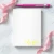 Overhead view of a Holla Swash rectangular notepad with a lemon-yellow script name in the lower-right corner, styled with pink ribbon and a pen.