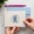 Personalized folded notecard held in both hands, showing the A2 card size, navy and light blue monogram, and coordinating blue envelope.