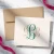 Classic folded monogram notecard personalized in green and tan with a coordinating neutral envelope on a bright marble desk.