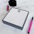 Gray-bordered personalized square notepad with black monogram, pink pen, and ink bottle
