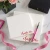 Two Holla Swash square notepads with red script names, styled with pink ribbon, flowers, a fountain pen and a black box.