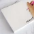 Close-up of a hand holding a pink fountain pen over a Holla Swash square notepad with a black script name in the lower-right corner.