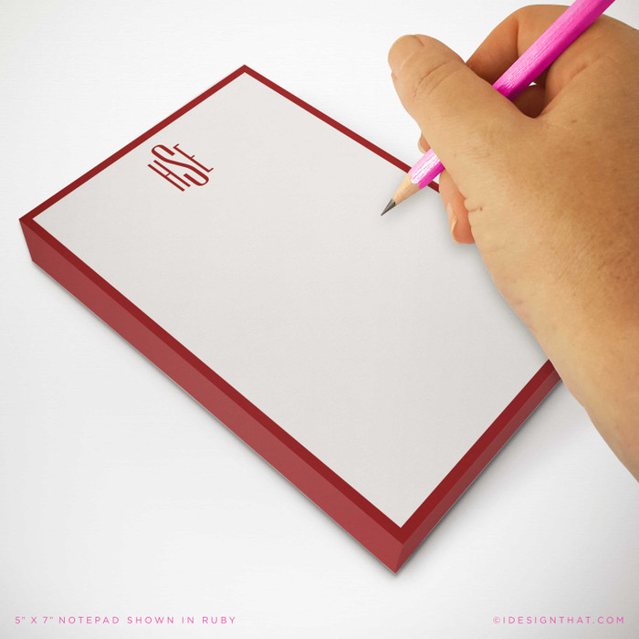 Person writing on personalized monogram notepad with ruby red border; slim, modern design for professional desks or gifting