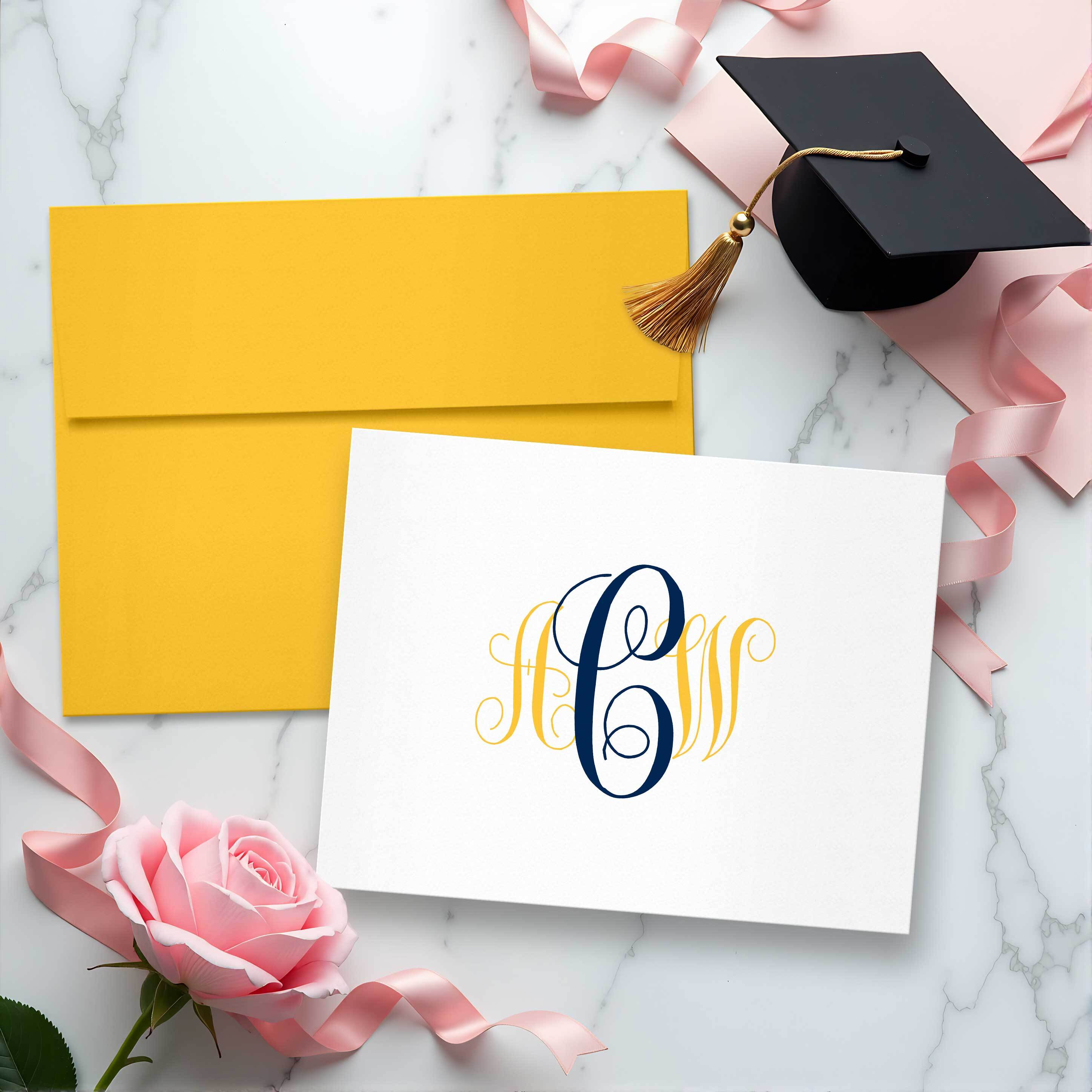 Graduation stationery flat lay with personalized monogrammed notecard, gold envelope, pink ribbon, and graduation cap — custom gift idea for grads