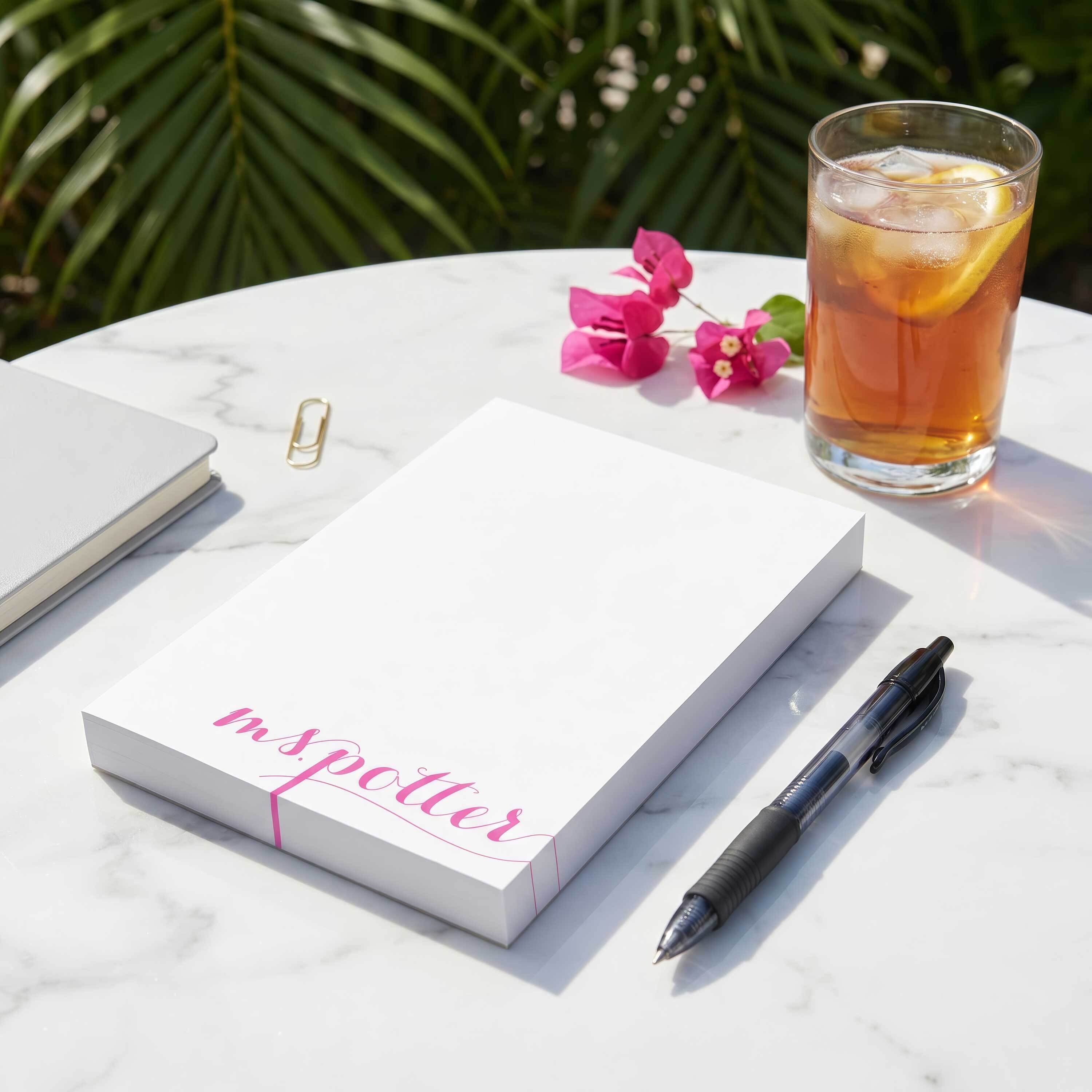 Personalized teacher notepad with pink script name on a marble table, styled with iced tea and pen for a useful teacher gift
