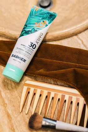 sunscreen tube laying next to makeup brush and comb