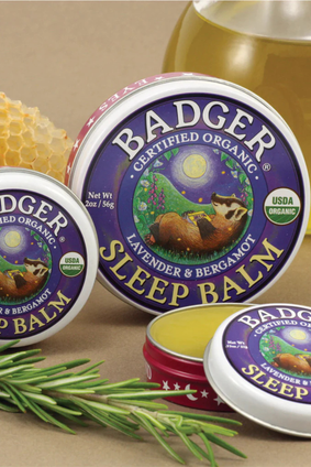 badger sleep balm tin sitting on table with beeswax and rosemary