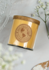 A golden brown candle lays on its side next to a wooden spoon sprinkled with flour, a crystal cake platter, and a sprig of baby's breath.