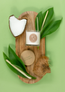 A white soy candle lays on its side surrounded by chunks of coconut and stalks of lemongrass atop a wooden cutting board.