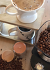 Hot coffee is dripping next to a grinder filled with freshly roasted beans and an Eco soy Coffee Bean candle at the center of the kitchen table.