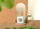 A pale green Eco soy candle rests on a cork coaster alongside a stem of eucalyptus with greenery in the foreground.