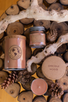 Overhead view of an assortment of brown soy candles on a rustic wooden table, nestled among pine cones and knotty tree branches.