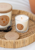 Freshly lit 6 oz white soy candle on a wicker tray with a black metal wick trimmer and larger white candle on a  white background.