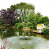 Installed PondJet Floating Fountain operating in a garden pond, with a central jet sending multiple arched streams of water about 6 feet high and secondary low sprays encircling it, surrounded by lush trees and a wood deck with seating.