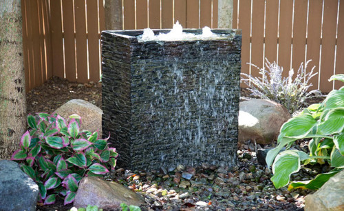 Installed stacked slate wall fountain mounted on an exterior wall with water flowing evenly down the slate surface into a decorative trough below. Installed stacked slate wall fountain mounted on an exterior wall with water flowing evenly down the slate surface into a decorative trough below.