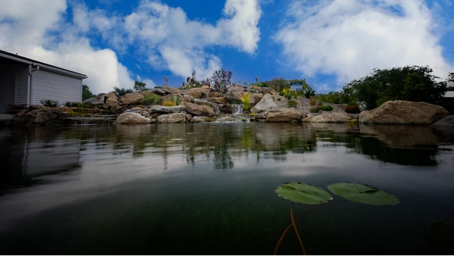Natural pond with a waterfall under a blue sky