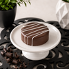 Classic chocolate covered sandwich cookie with white chocolate drizzle on a white pedestal, handcrafted by Bomb Confections.