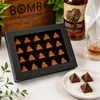 Twenty handcrafted Buffalo Trace Bourbon Bonbons by Bomb Confections presented in a premium black window gift box with three artisan chocolates displayed in front and subtle bourbon-inspired accents.