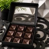 Open luxury gift box filled with nine handcrafted espresso chocolate bonbons featuring geometric square shells and smooth dark chocolate finish by Bomb Confections.